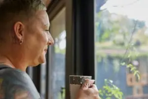 Woman looking out of a window into the garden, cup of coffee in hand